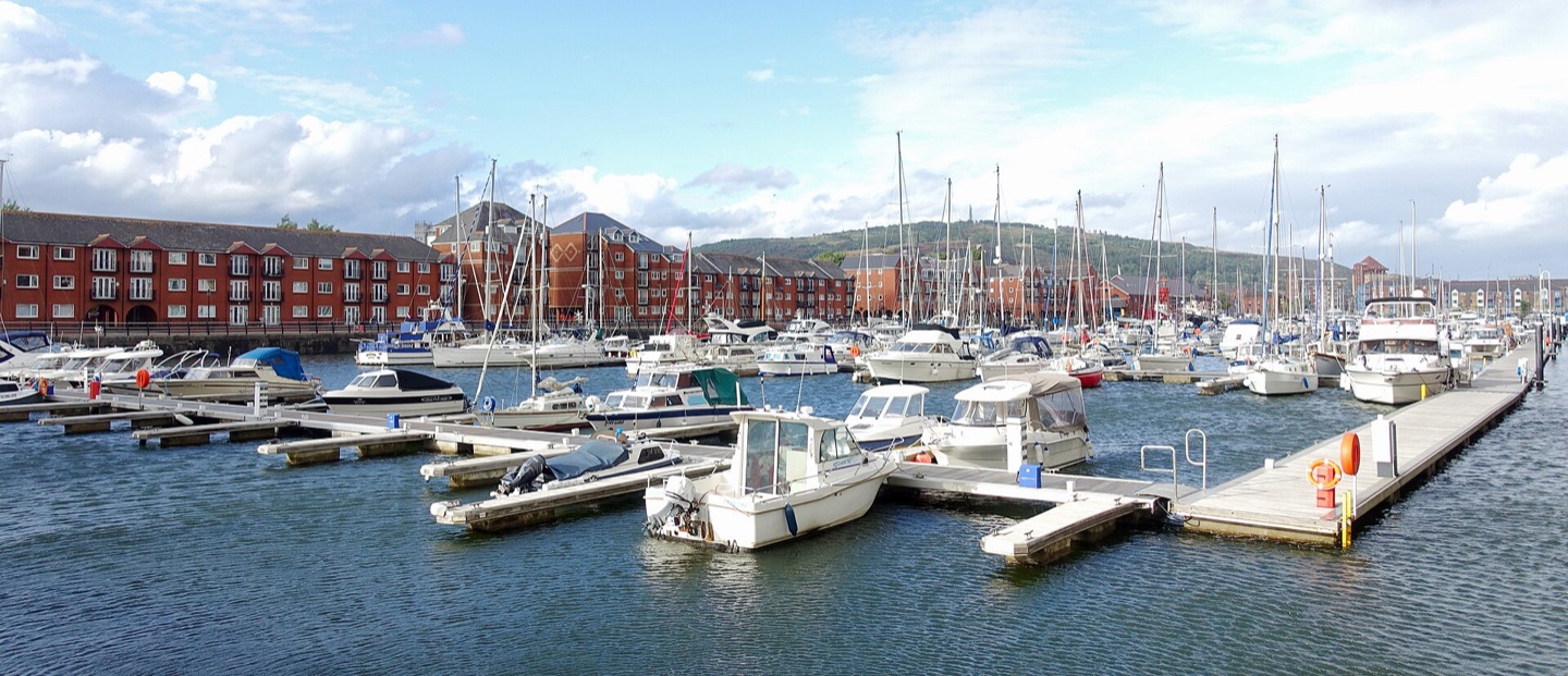 Yachts and motor boats moored at Swansea Marina, with waterside flats and hills behind